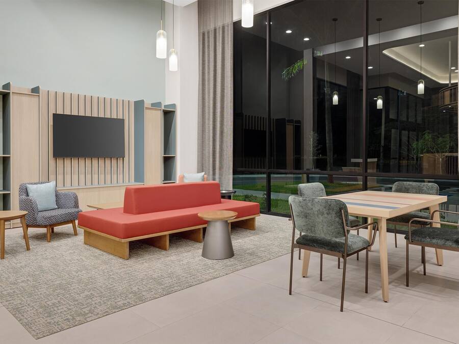 Un espace détente moderne avec un canapé rouge, des fauteuils gris, une table en bois et un téléviseur à écran plat fixé au mur.