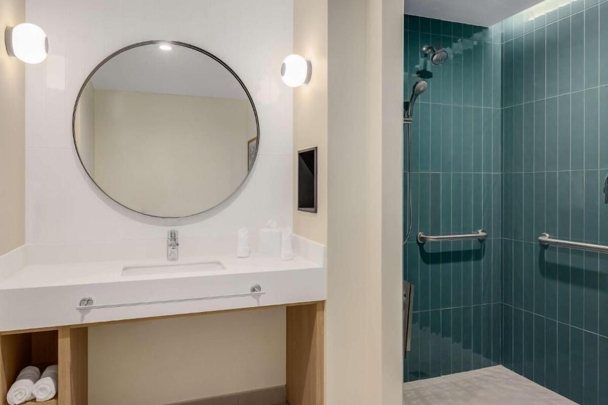 Een badkamer met een ronde spiegel, een witte wastafel en een douchegedeelte met blauwe tegels.