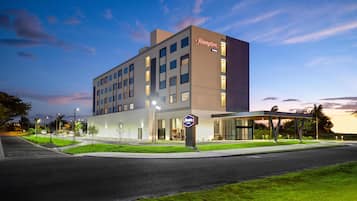 A modern hotel with a prominent 'Hampton' sign, featuring a clean, rectangular design with multiple windows and a flat roof.