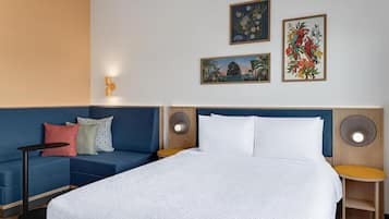 A hotel room with a large bed, a blue sofa, a small table, and two wall-mounted speakers.