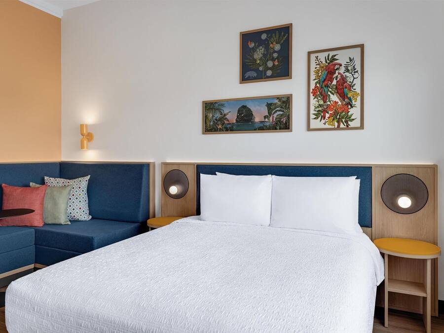 A hotel room with a large bed, a blue sofa, a small table, and two wall-mounted speakers.