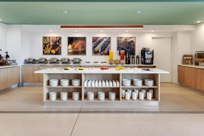 A modern kitchen area with a central island, multiple shelves with plates, and various food items.