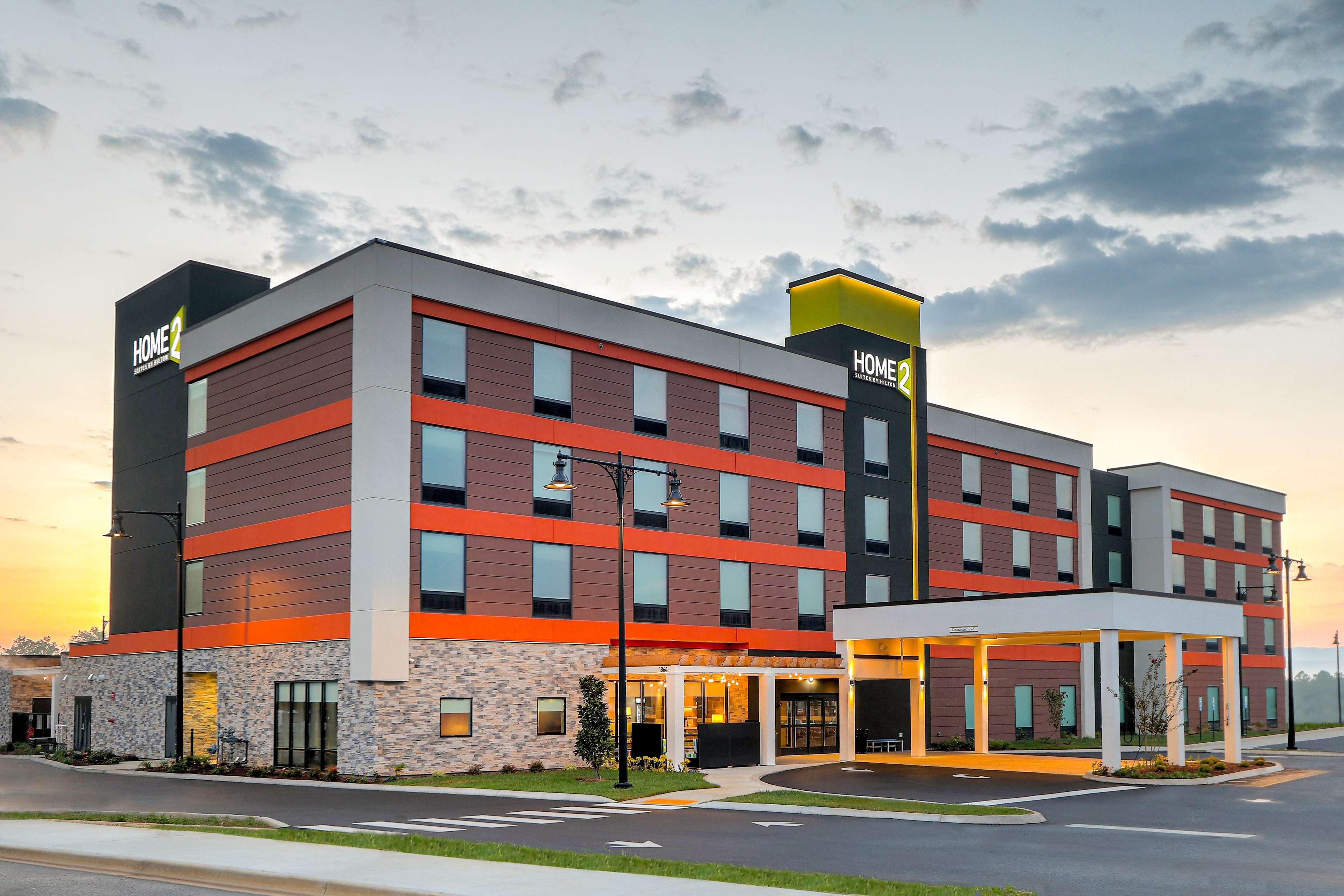 A multi-story hotel with a modern design, featuring a prominent "HOME2" sign, a covered entrance, and a landscaped front area.