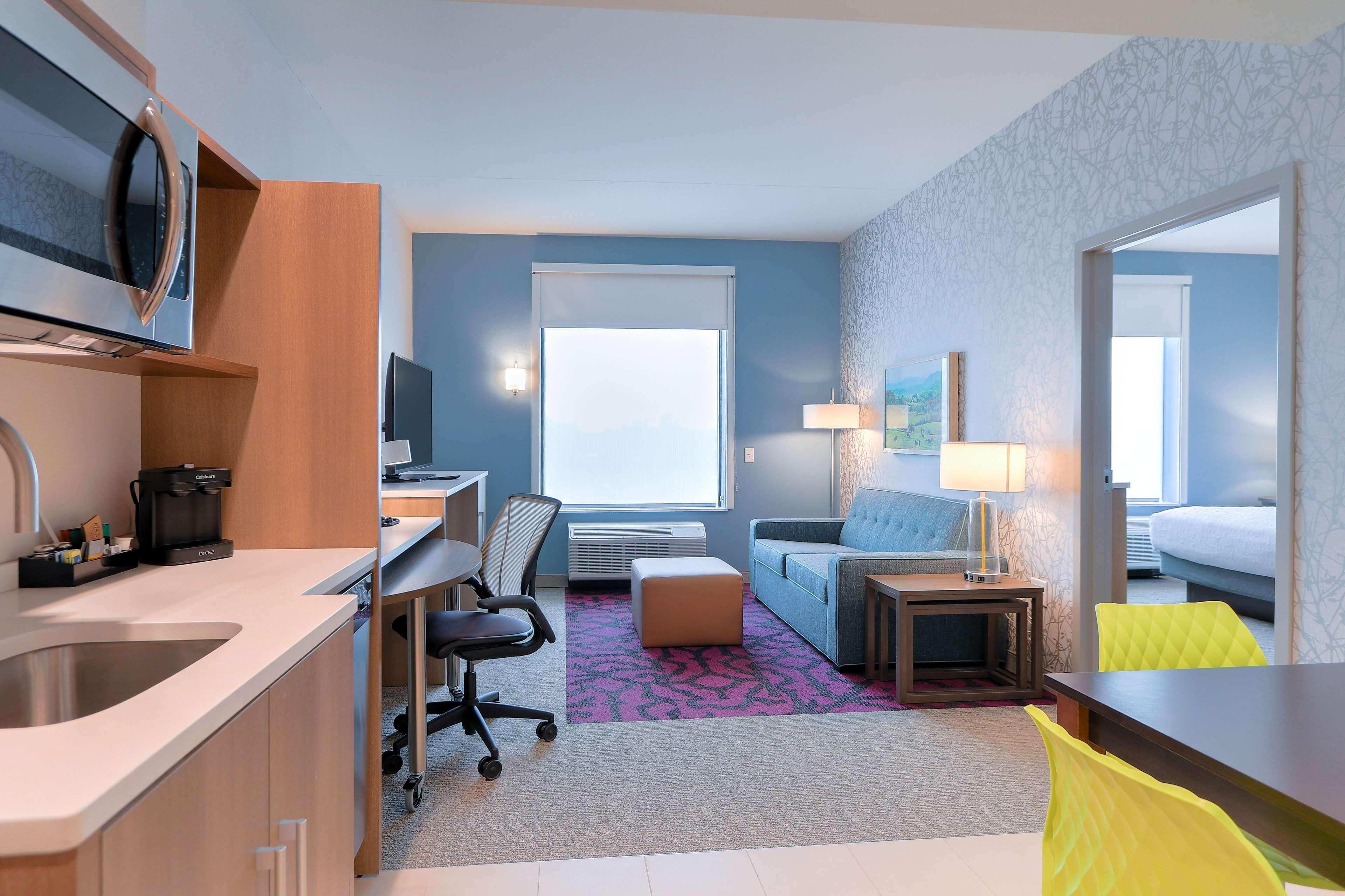 A compact hotel room with a kitchenette, a sofa, a small table, and a bed.