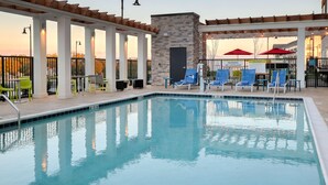 A pool area with a stone wall, blue chairs, and a sign warning of no lifeguard.