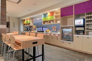 A modern restaurant with a wooden dining area, colorful shelving, and a self-service beverage station.