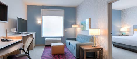 Ein Hotelzimmer mit Schreibtisch, Stuhl, Sofa, Nachttisch, Lampe und einem Bett.
