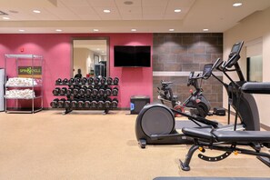 A gym with exercise equipment, a wall-mounted TV, and a rack of dumbbells. - Home2 Suites By Hilton Alcoa Knoxville Airport (Alcoa)