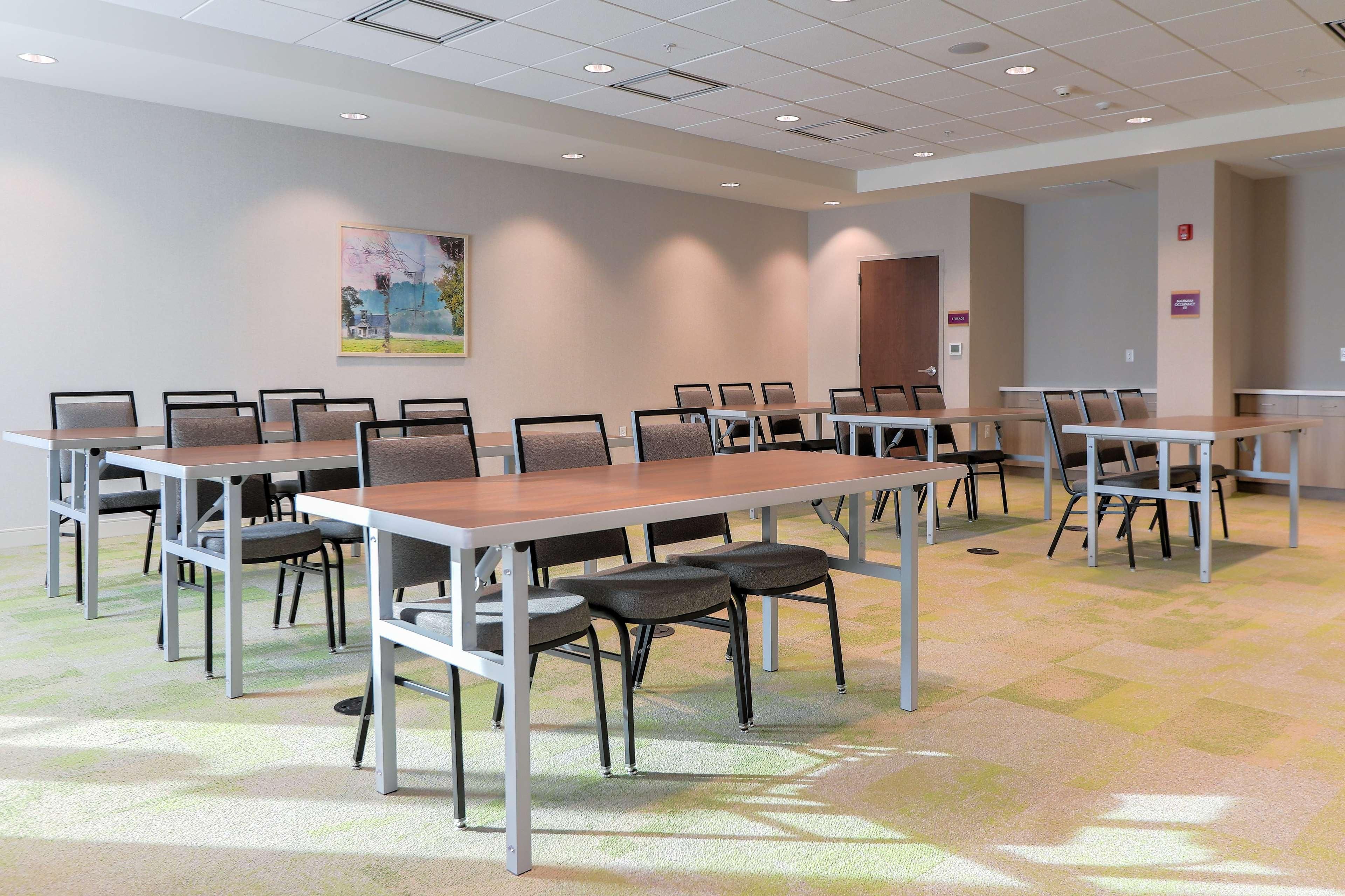 A conference room with multiple tables and chairs, carpeted flooring, and a painting on the wall.