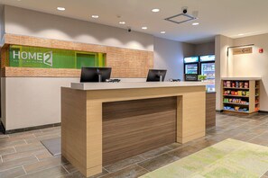 A hotel reception desk with a "HOME 2 SUITES BY HILTON" sign, a computer station, and a snack vending machine. - Home2 Suites By Hilton Alcoa Knoxville Airport (Alcoa)