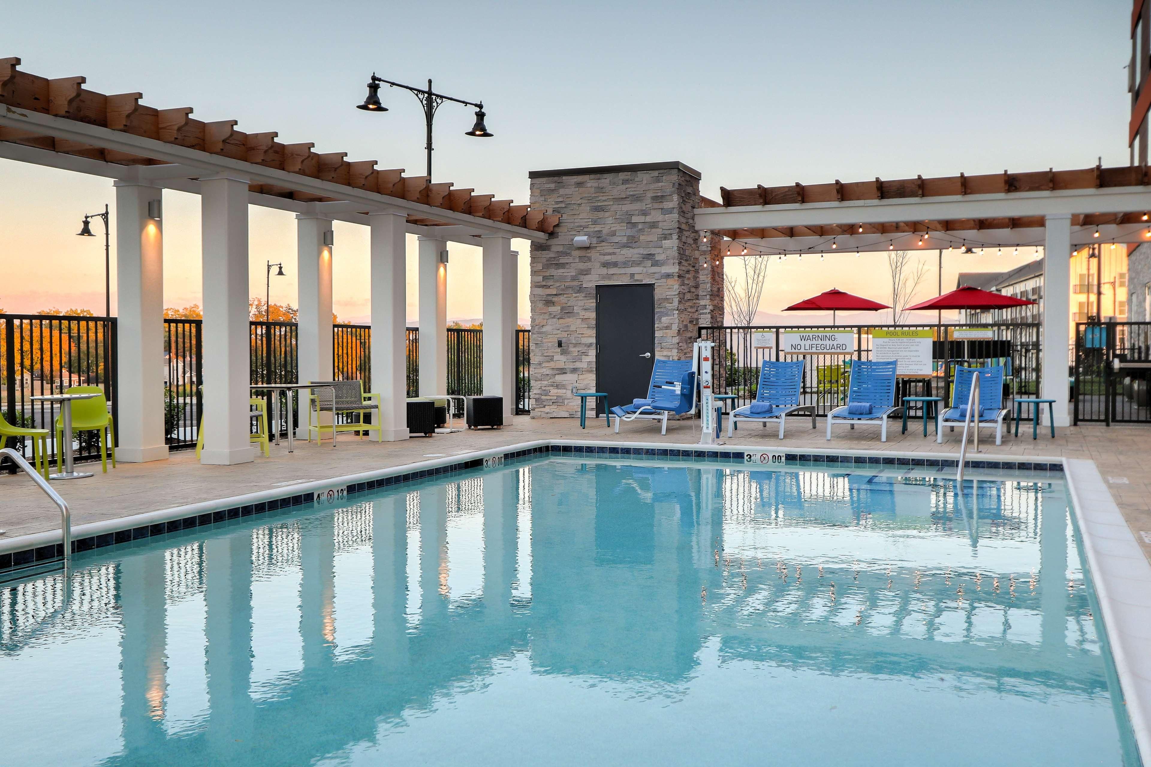A pool area with a stone wall, blue chairs, and a sign warning of no lifeguard.