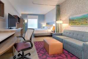 Habitación de hotel con cama, sofá, escritorio con computadora, televisor y un cuadro en la pared.