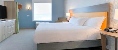 Habitación de hotel con una cama grande, una mesita de noche con teléfono, un escritorio con televisor y una ventana con vistas.
