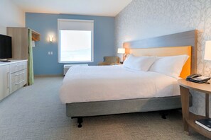 A hotel room with a large bed, a bedside table with a phone, a desk with a TV, and a window with a view. - Home2 Suites By Hilton Alcoa Knoxville Airport (Alcoa)