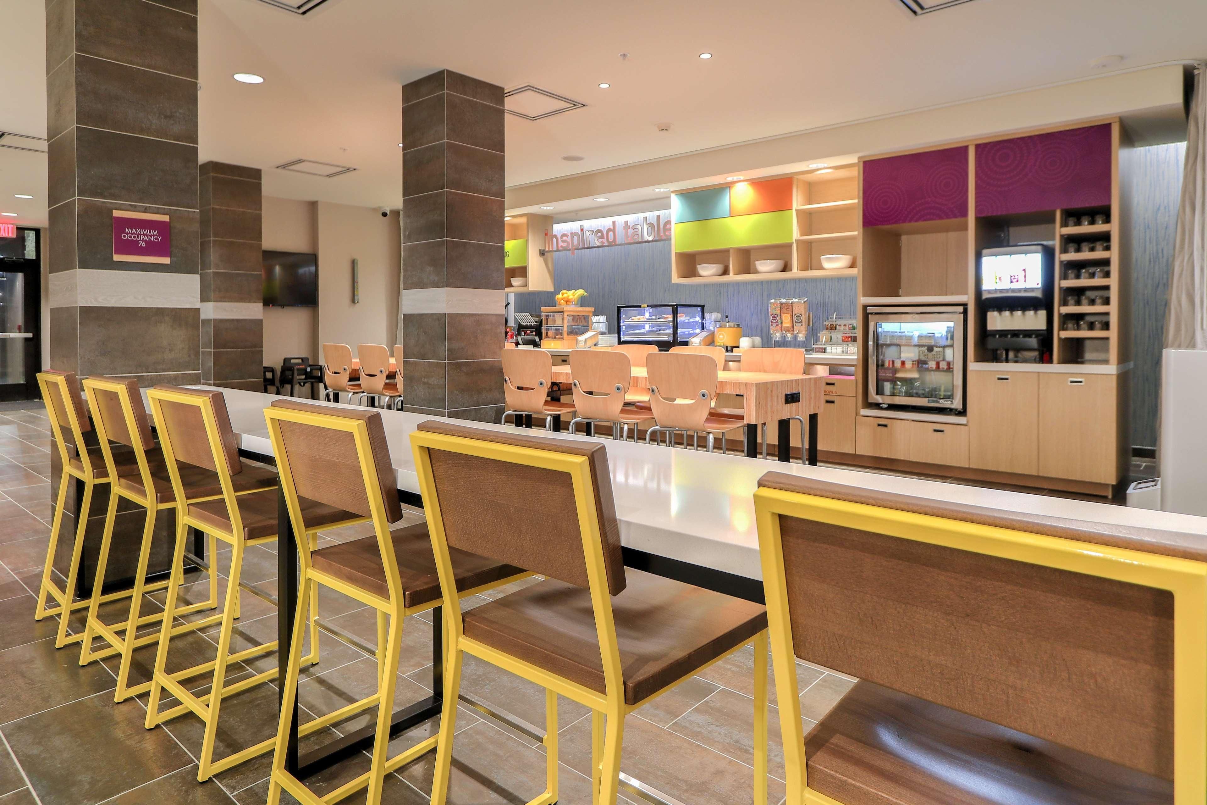A modern restaurant with a bar area, seating, and a kitchen in the background.
