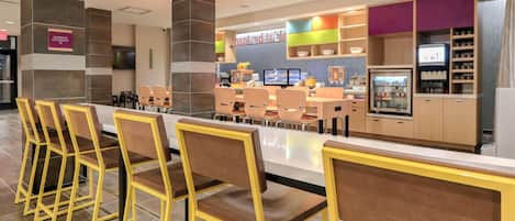 A modern restaurant with a bar area, seating, and a kitchen in the background.