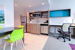 A modern kitchen with a microwave, sink, and dishwasher, a dining area with a table and chairs, and a desk with a chair. - Home2 Suites By Hilton Alcoa Knoxville Airport (Alcoa)