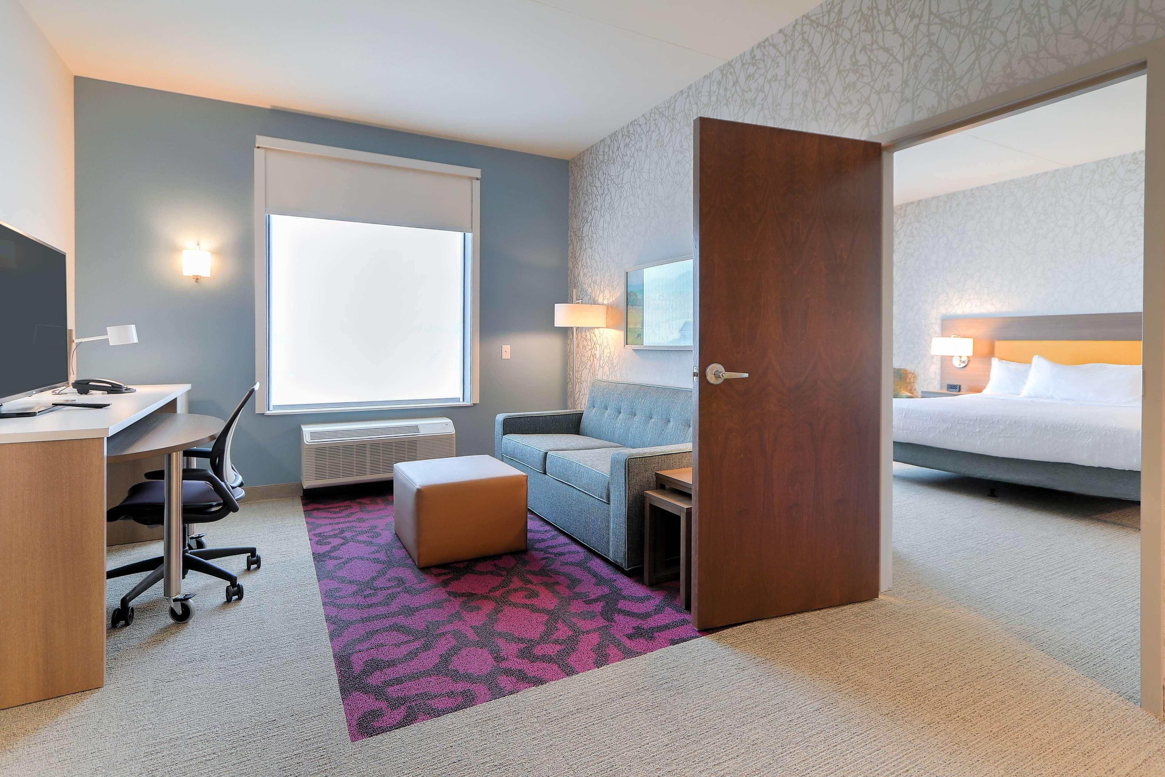 Una habitación de hotel con escritorio, silla, sofá, otoman y cama.