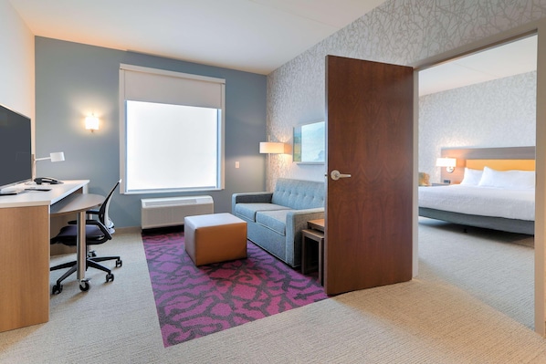 A hotel room with a desk, chair, sofa, ottoman, and a bed.