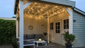 Een gezellig buitenterrein met een bank en bijzettafeltje, hangende lichtjes erboven en potplanten.