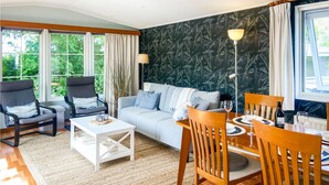 Een woonkamer met een bank, twee fauteuils, een salontafel en een eettafel met stoelen.