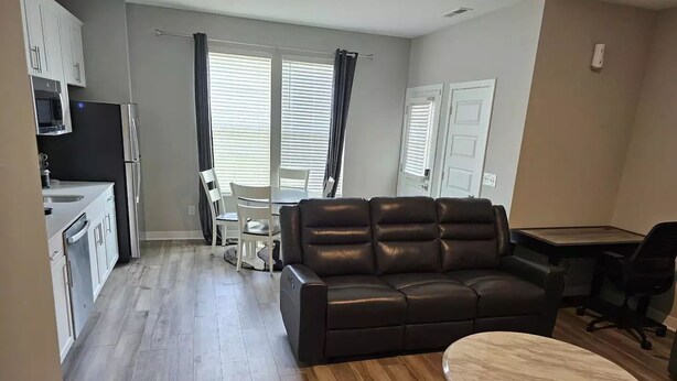 A modern living room with a brown leather sofa, a round wooden coffee table, and a dining area with a white table and chairs.