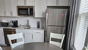 A modern kitchen with white cabinets, stainless steel appliances, and a round dining table with white chairs.