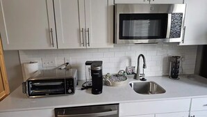A modern kitchen with white cabinets, a stainless steel microwave, a coffee maker, and a dishwasher.