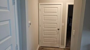 A hallway with a white door, a light switch, and a power outlet on the wall.