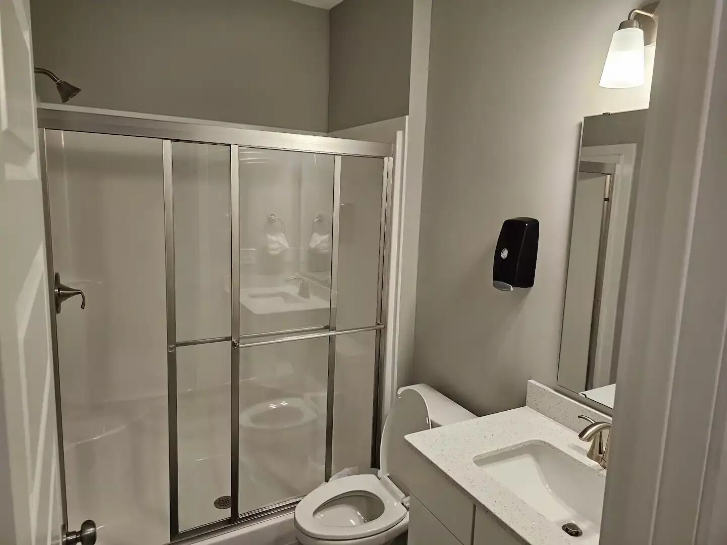 A bathroom with a glass-enclosed shower, a toilet, a sink, and a hand dryer.