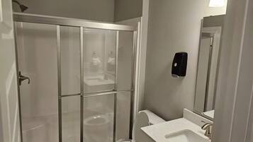 A bathroom with a glass-enclosed shower, a toilet, a sink, and a hand dryer.