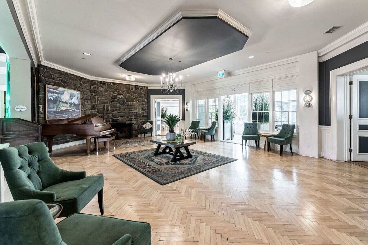 A spacious lobby with a grand piano, green upholstered chairs, a herringbone wood floor, and a stone accent wall.