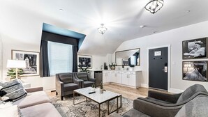 Uma sala de estar moderna com um sofá, poltronas, uma mesa de centro e um espaço de jantar com cozinha ao fundo.