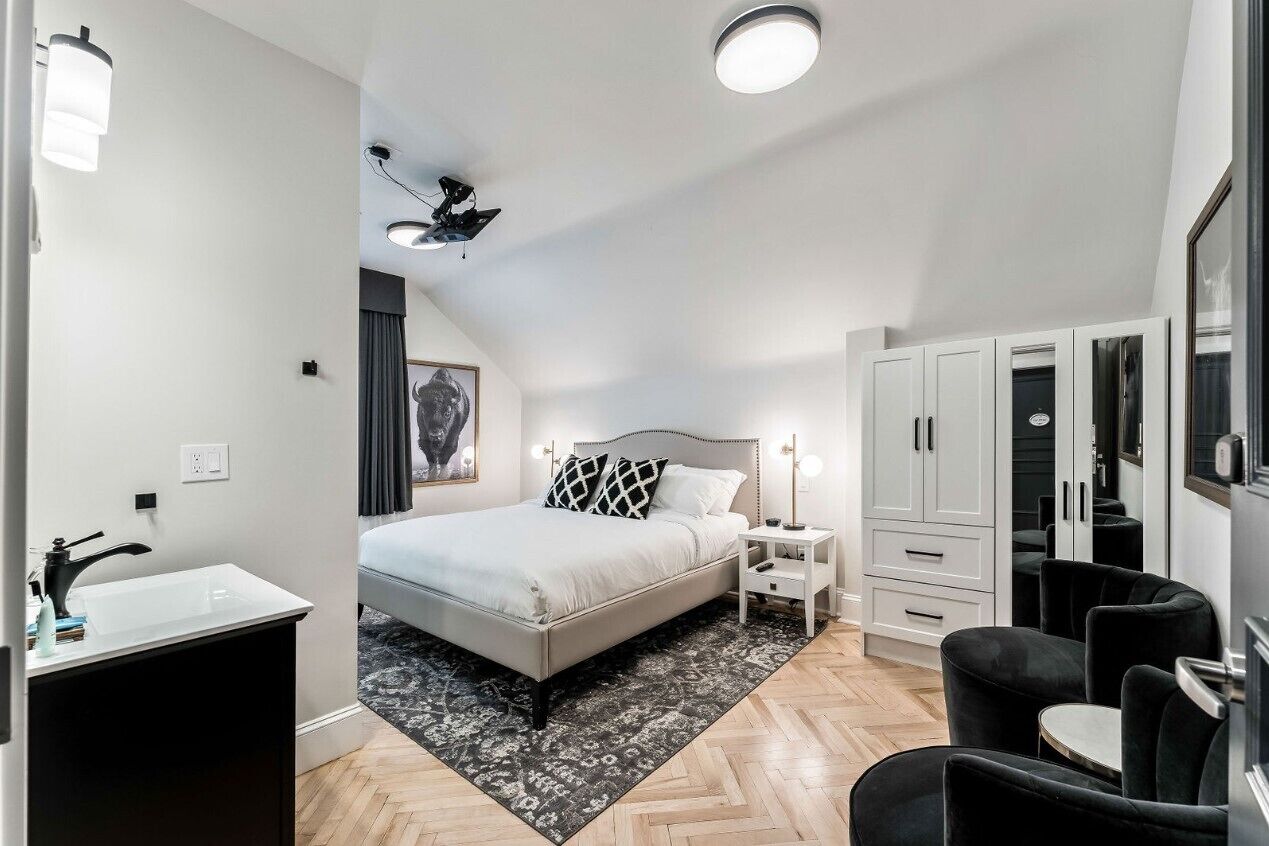 Un dormitorio moderno con cama, mesita de noche, armario y una pequeña zona de estar.