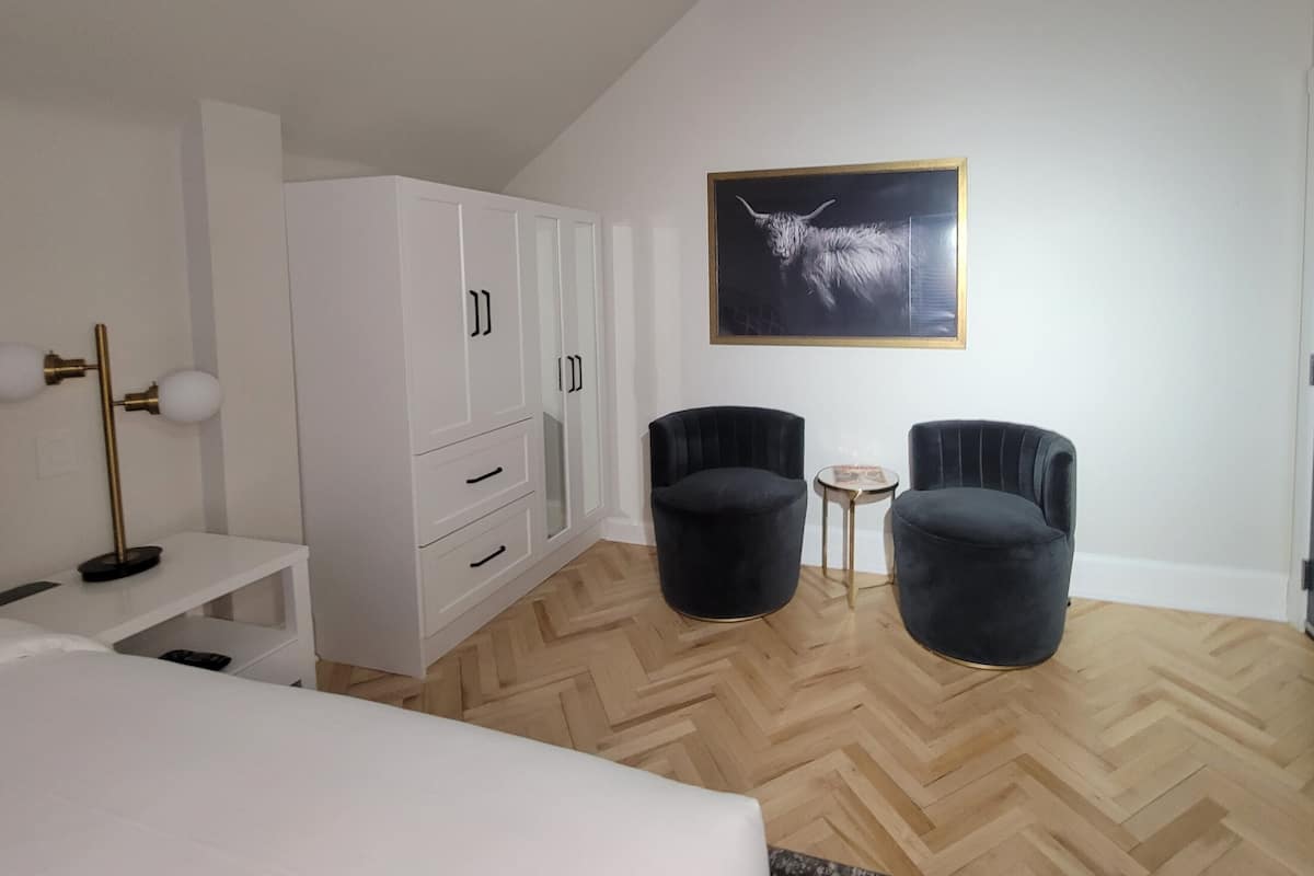 A modern bedroom with a white wardrobe, two black armchairs, a small round table, and a ceiling light fixture.