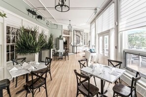 A spacious dining area with marble tables and dark wooden chairs, large windows, and potted plants. - The Inn on Officers Garden (Calgary)