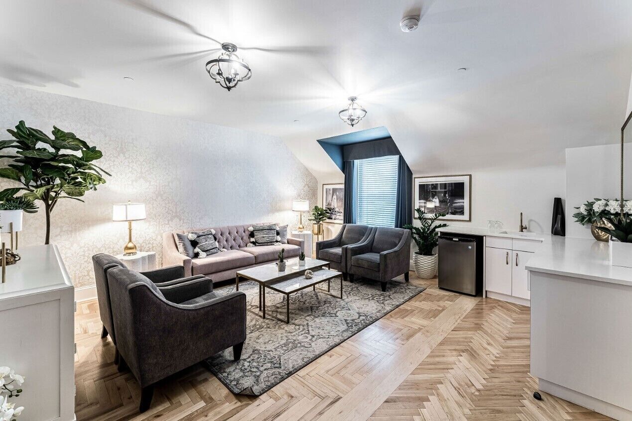 Una sala de estar moderna con un sofá, sillones, una mesa de centro y una zona de cocina con lavavajillas.
