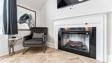 Ein Wohnzimmer mit Kamin, einem schwarzen Ledersessel, einem gerahmten Kunstwerk und einem an der Wand befestigten Fernseher.