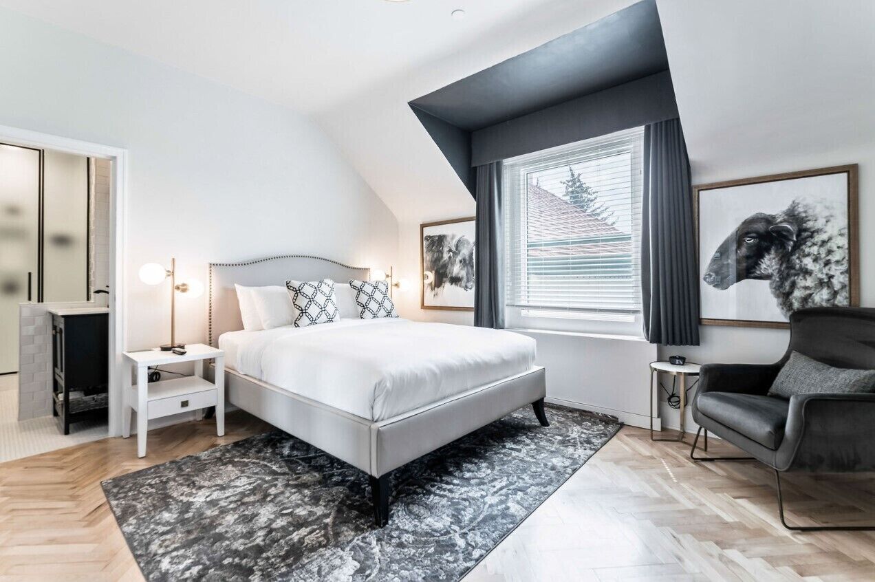 A modern bedroom with a large bed, a side table, a chair, and a window with a view.