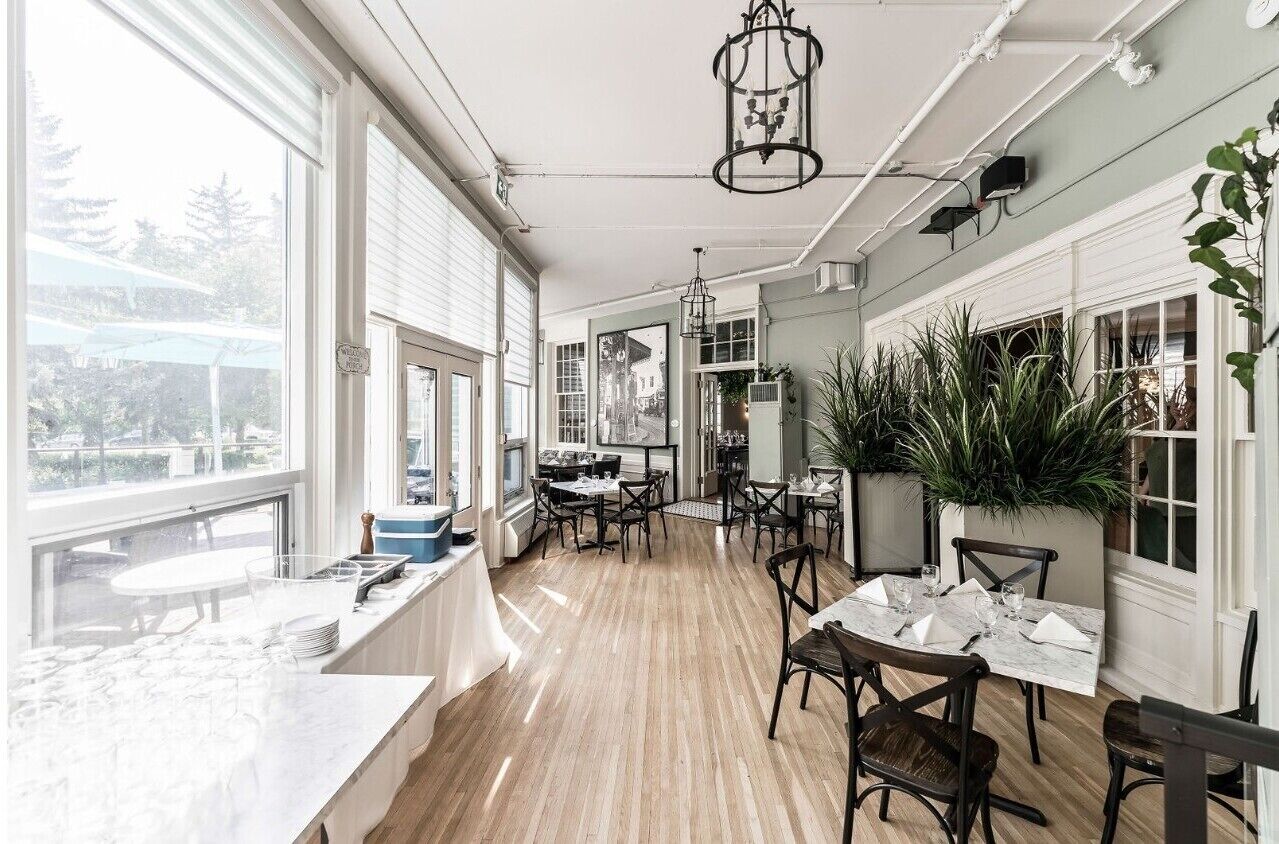 A bright, open dining area with wooden flooring, large windows, and a variety of seating arrangements.