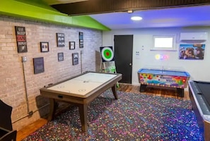 A room with a foosball table, a pool table, and a dartboard.