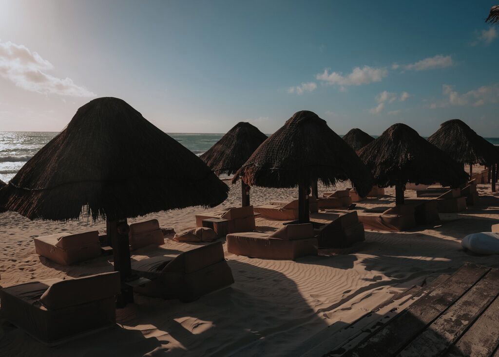 A beach with thatched umbrellas and wooden lounge chairs.