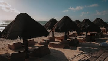 Una playa con sombrillas de paja y sillones reclinables de madera.