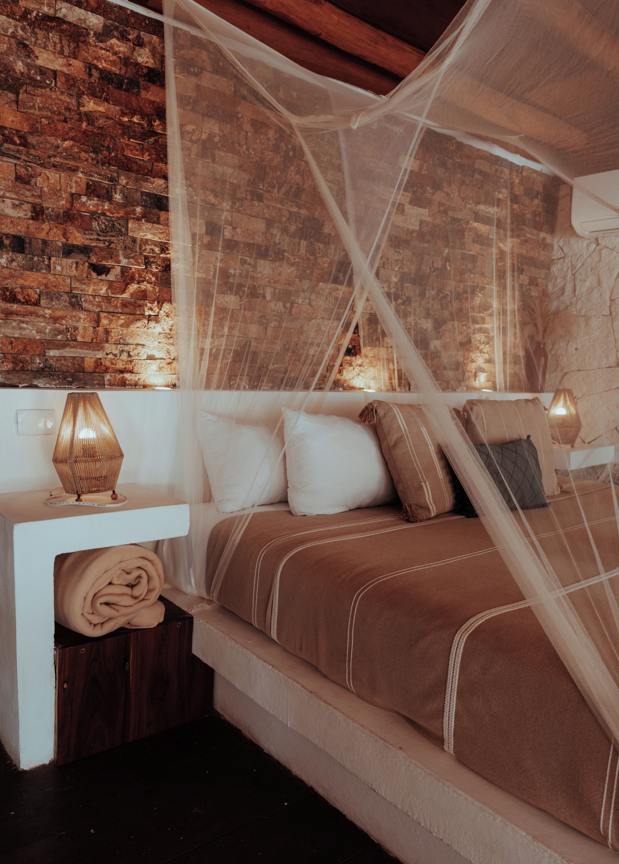 Un dormitorio con pared de ladrillo, una cama con dosel y una mesita de noche con lámpara.