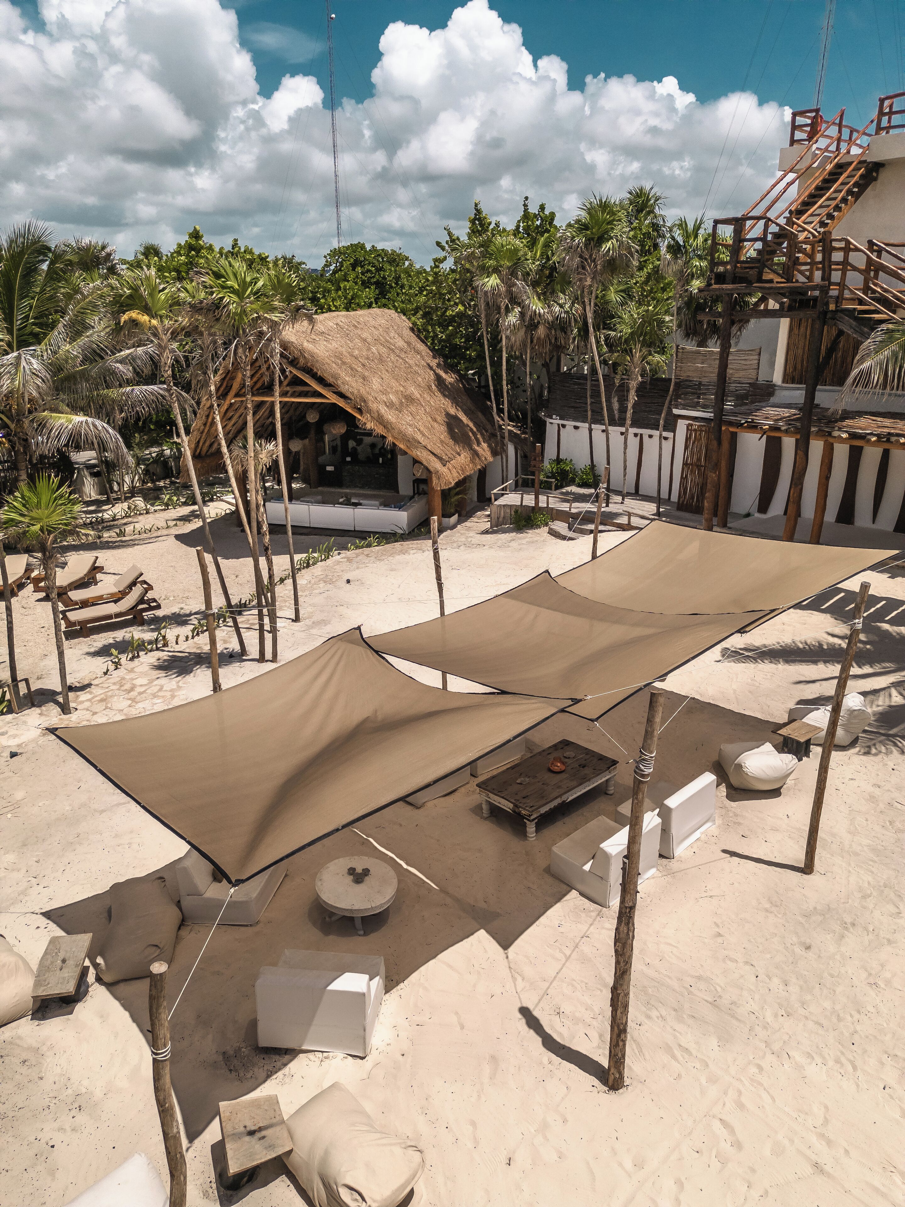 A beach area with a large thatched-roof structure, lounge chairs, and a sandy floor.