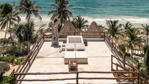 Vista de una playa con una estructura de techo de paja, sillas de descanso y palmeras.