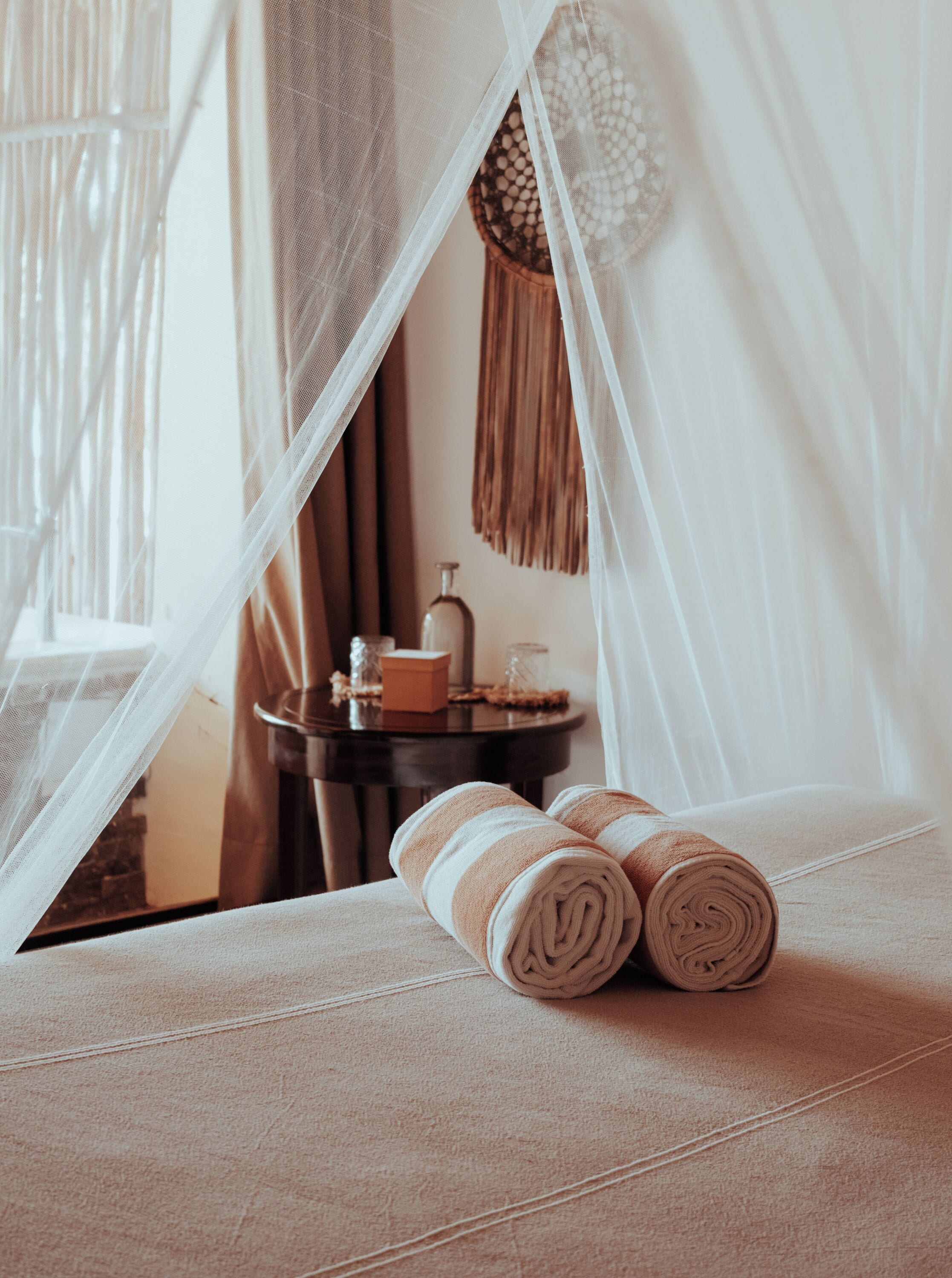 A cozy room with a bed, a bedside table, and a window with sheer curtains.