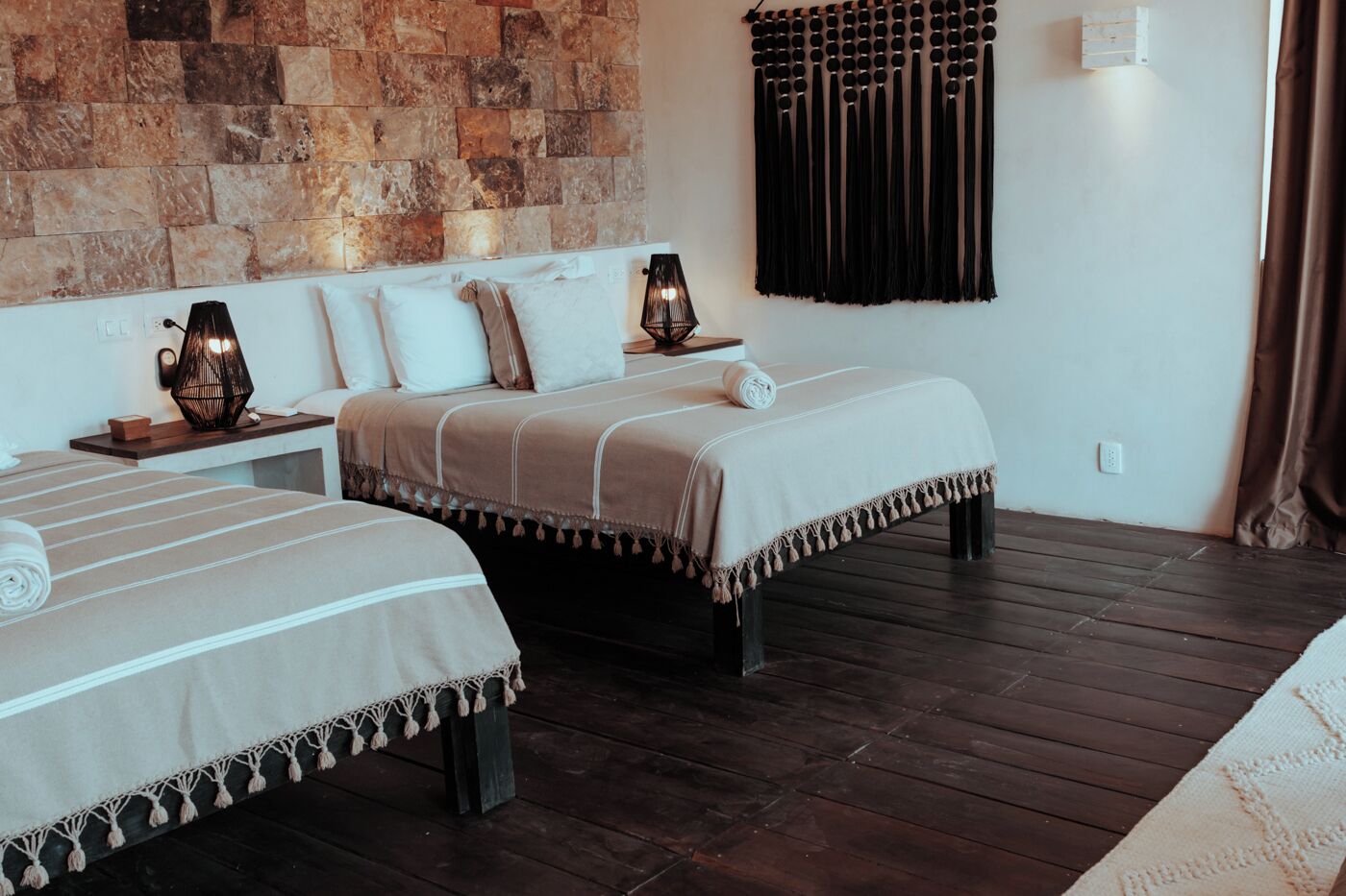 Ein Hotelzimmer mit zwei Betten, einer Steinwand, einem schwarzen Vorhang und einem Holzboden.