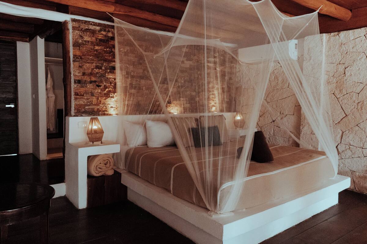 Un dormitorio con cama bajo dosel, una mesita de noche con lámpara y una pared de ladrillo.