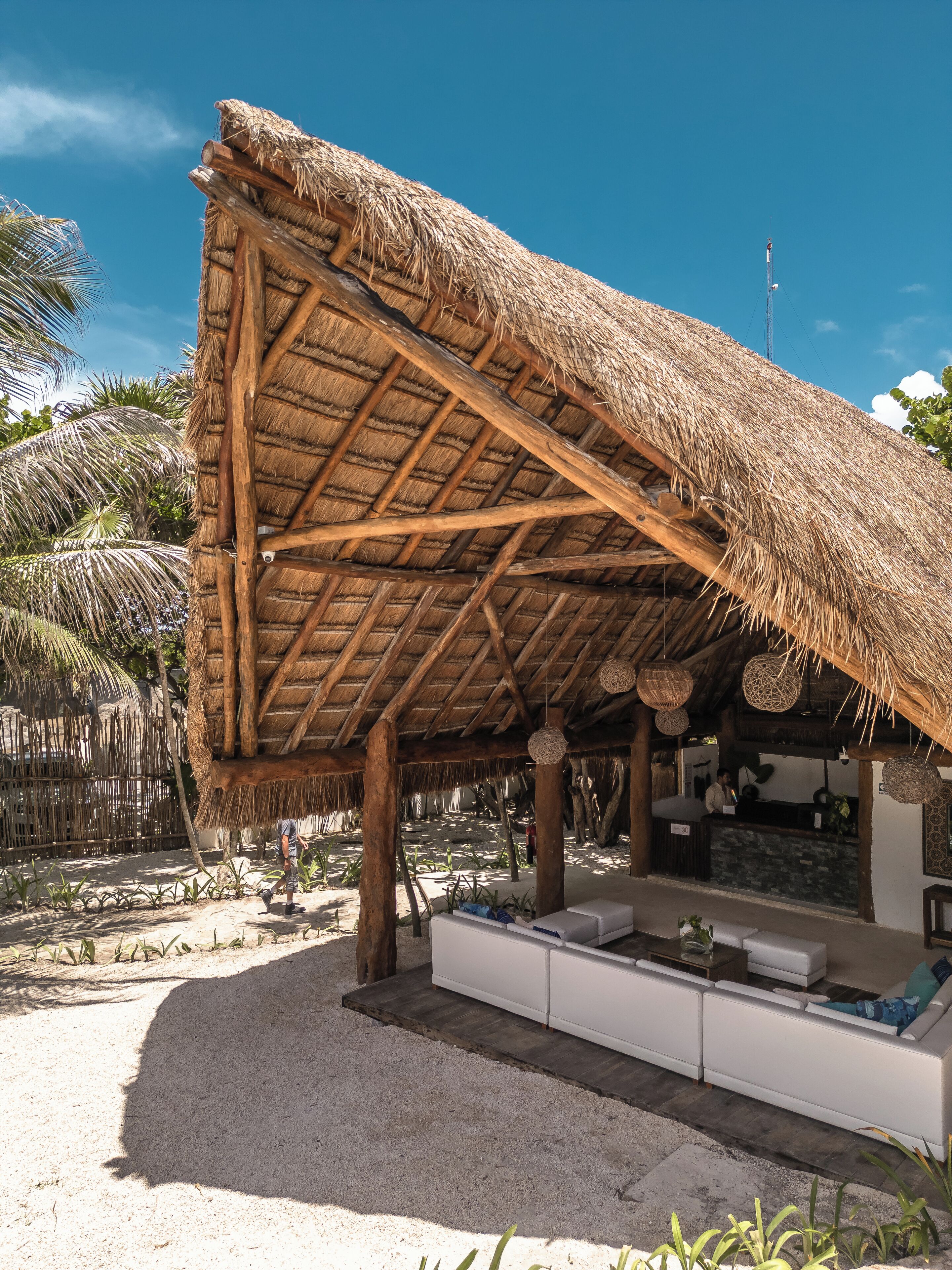 A thatched-roof structure with a sandy floor and white seating area.
